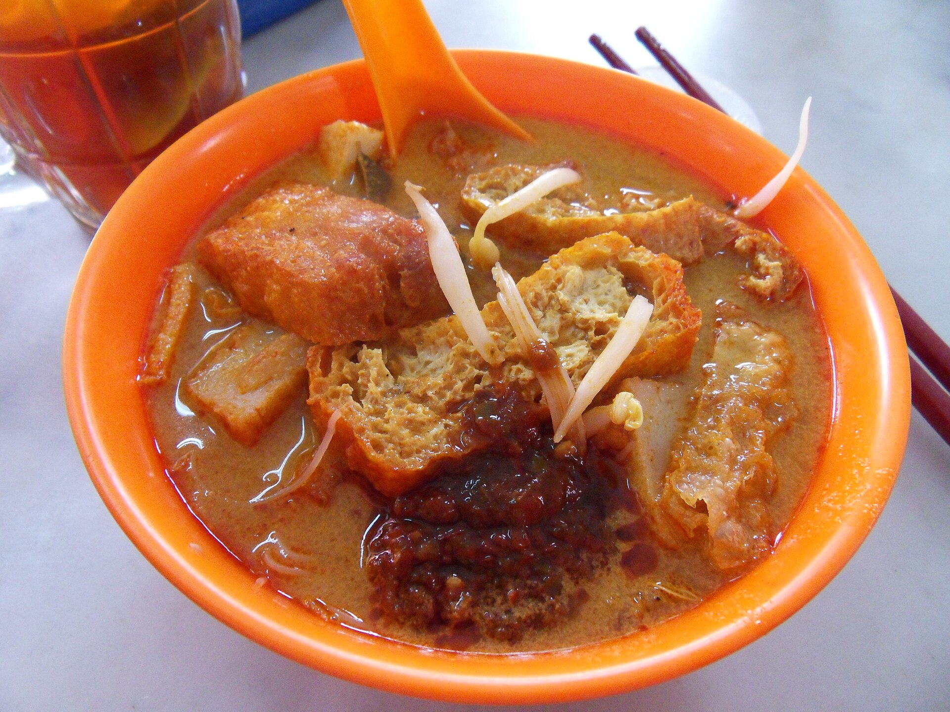 Curry laksa in an orange bowl with tofu puffs and bean sprouts.